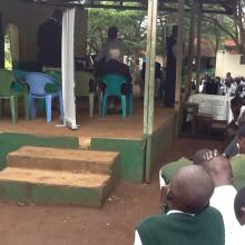 Children taking part in an online inter-school debate. The children are seeing images of the other school on a big screen.