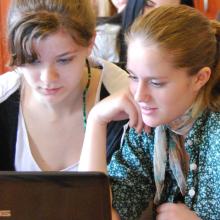 Two teenaged girls researching the internet on a desktop computer.