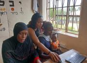 Women learning to use computers at a previous ICT camp in Uganda. One of the women has a baby on her lap.