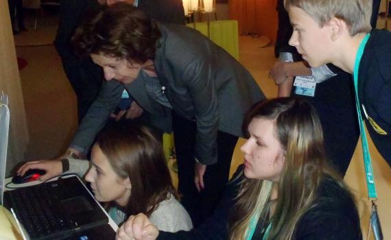 Children show Ms Neelie Kroes how to access and play the game on computers.