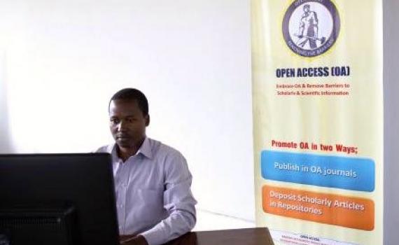 A student in the library at a computer. Behind him is an OA banner.