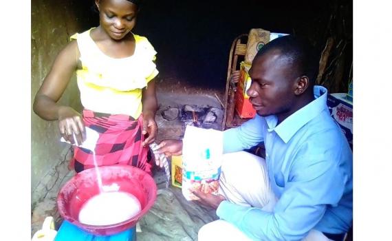 Zariakah Kyozira practising new baking skills at home, watched by Isa Maganda, Isa Maganda, Chief Librarian at Nambi Sseppuuya Community Resource Centre in Uganda.